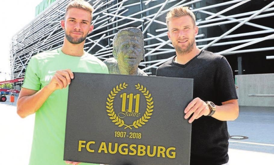 FCA-Nachwuchstalent Simon Asta (links) und Kapitän Daniel Baier freuen sich auf noch viele Aktionen und Feierlichkeiten rund um das 111-jährige Jubiläum des FC Augsburg. Hier präsentieren sie das eigens entworfene Jubiläums-Logo des Vereins. Foto: FC Augsburg FCA-Nachwuchstalent Simon Asta (links) und Kapitän Daniel Baier freuen sich auf noch viele Aktionen und Feierlichkeiten rund um das 111-jährige Jubiläum des FC Augsburg. Hier präsentieren sie das eigens entworfene Jubiläums-Logo des Vereins. Foto: FC Augsburg