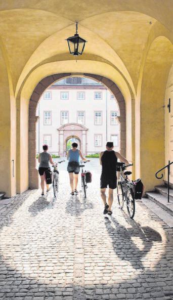Drei Radfahrer schieben zum Abschluss der „Fährmann, hol über“-Tour ihre Drahtesel durch den Eingang des Klosters Corvey in Höxter. Foto: IMAGO/Dieter Mendzigall