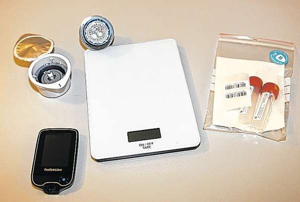 Im Testpaket befindet sich der steril verpackte Blutzuckersensor (links oben), eine Waage, zwei Röhrchen für die Stuhlproben (rechts) und ein Lesegerät (vorne links). Im Testpaket befindet sich der steril verpackte Blutzuckersensor (links oben), eine Waage, zwei Röhrchen für die Stuhlproben (rechts) und ein Lesegerät (vorne links).